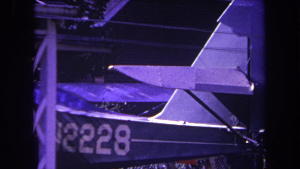 1969 Yucaipa home-movie frame showing a small aircraft parked under a covered structure, with N2228 visible on the fuselage.