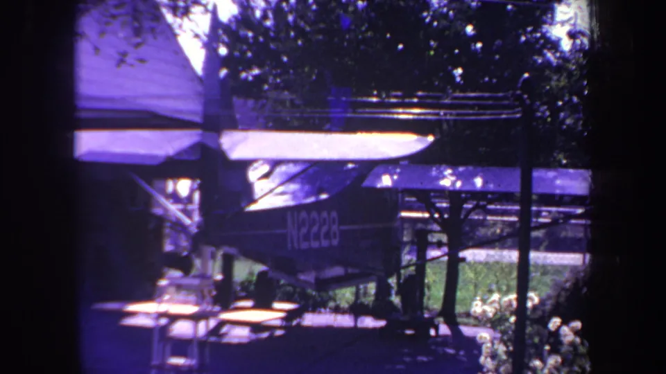 Final frame shows the same small aircraft parked beneath the cover, with trees and yard foliage in the background.