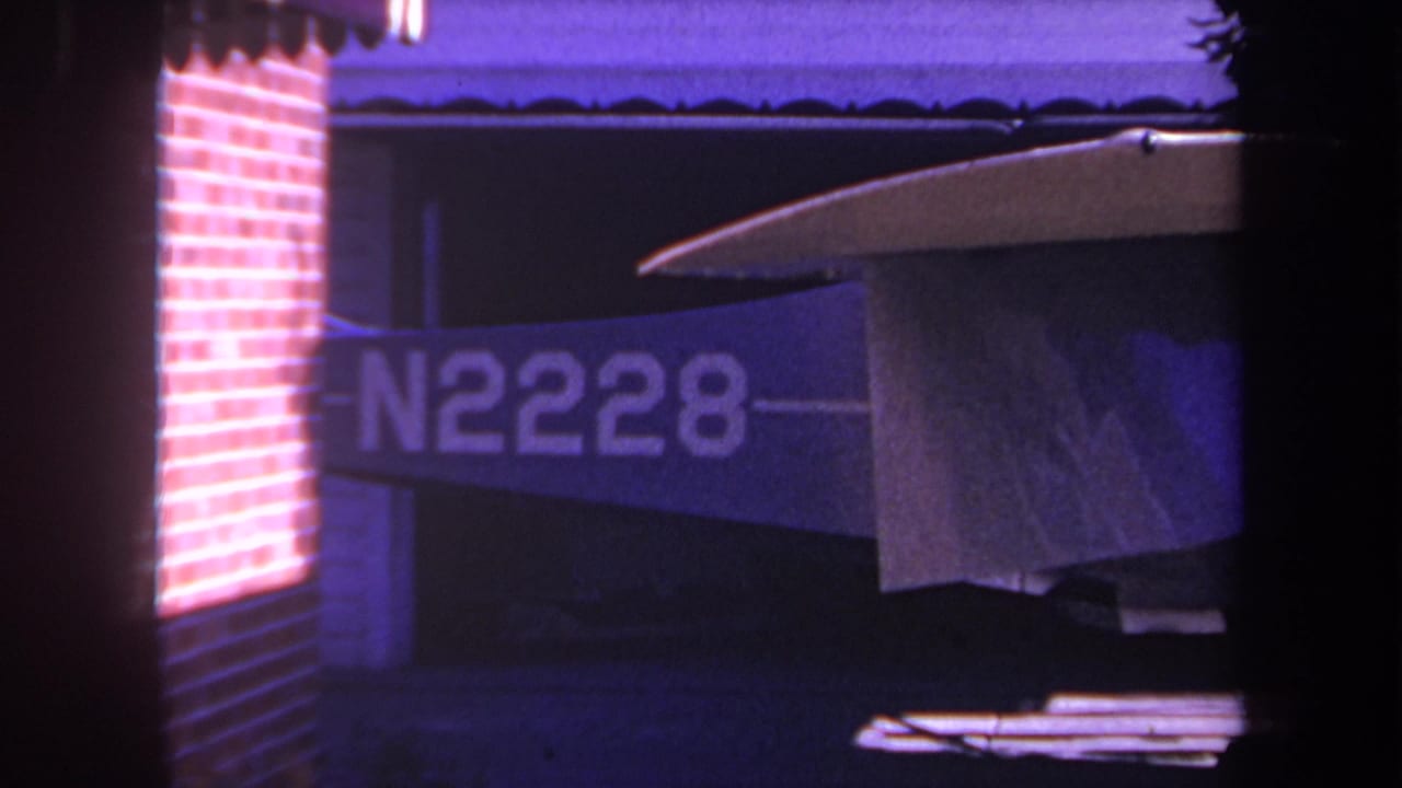 1969 Yucaipa, California 8mm frame showing a small aircraft tail section with N2228 visible, a brick wall at left, and purple-tinted film color.