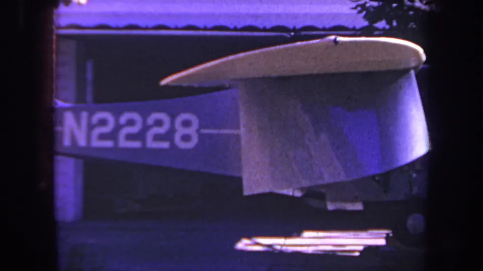 1969 Yucaipa, California 8mm frame with the small aircraft tail and N2228 registration centered against a building exterior under purple-shifted exposure.