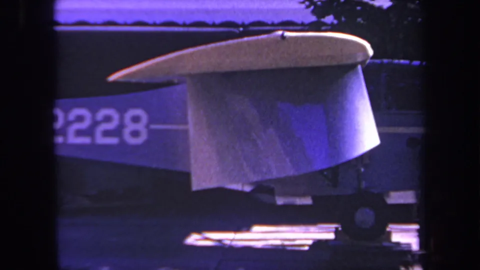 1969 Yucaipa, California 8mm frame showing a cropped aircraft tail, partial registration numerals, rear fuselage, wheel, and sunlit ground detail.