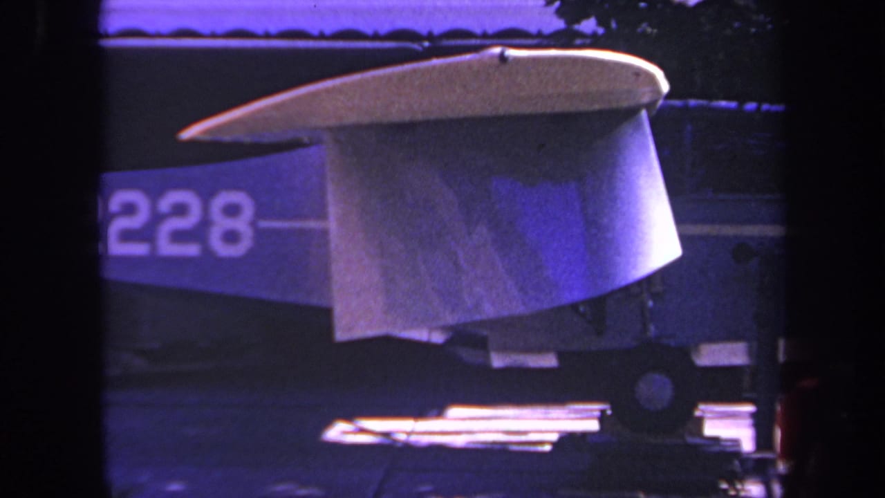 1969 Yucaipa home-movie frame showing a white homebuilt aircraft tail section with partial N2228 marking and dark background.