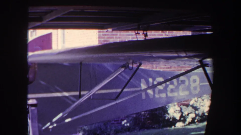 1969 8mm frame from Yucaipa showing a closer side view of the parked small aircraft, with wing struts crossing the fuselage and the registration partially visible.