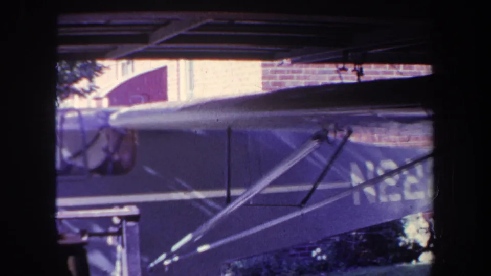1969 Yucaipa home-movie frame showing the side of a small aircraft under a garage or hangar opening, with wing struts and a partial N2228 registration visible.