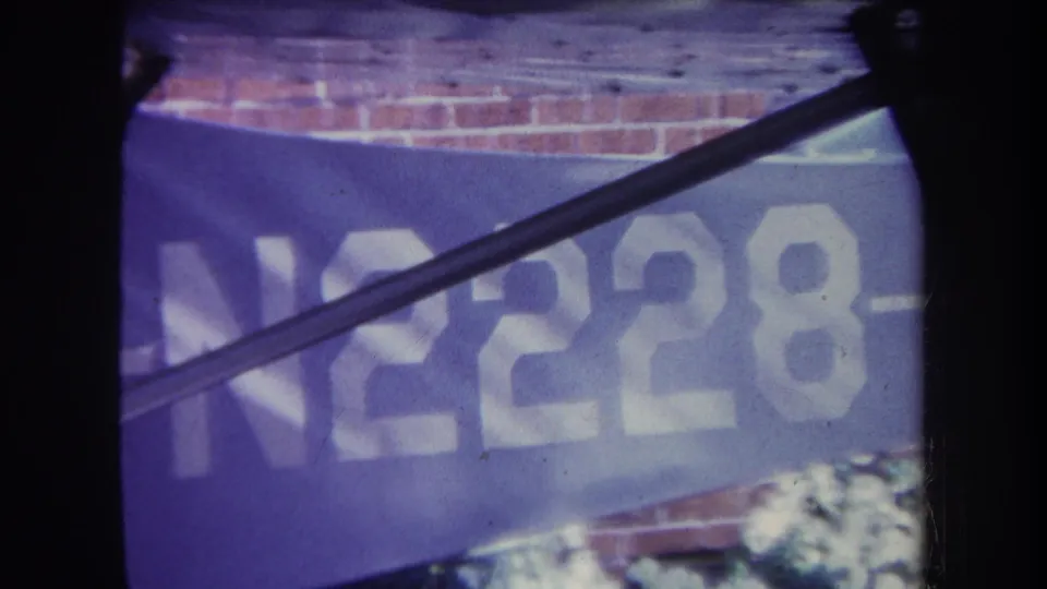 Close 1969 Yucaipa frame of the aircraft fuselage showing the large registration marking N2228, with a wing or strut crossing the frame and brickwork in the background.