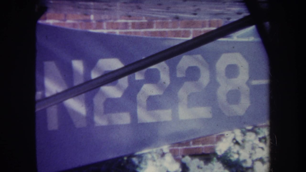 Close view of blue aircraft lettering N2228 with brick wall behind and dark framing edges.