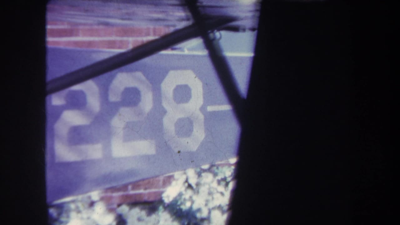 Blue banner with white 228 lettering against a brick wall, partly blocked by dark framing and a diagonal bar.