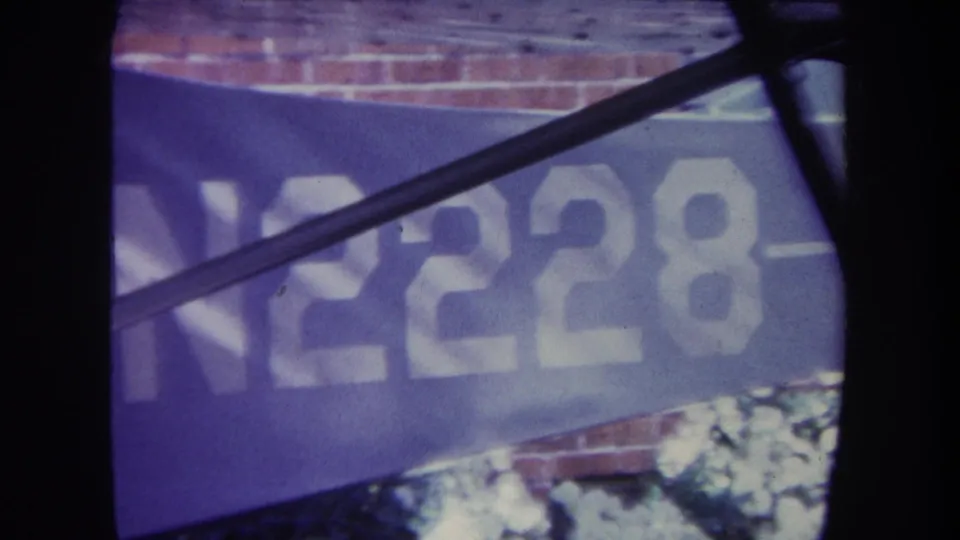 1969 Volmer Yucaipa home-movie frame showing the blue banner more clearly, with white N2228 lettering partly obscured by a diagonal metal bar.