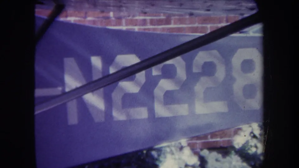 Final 1969 8mm frame showing the blue N2228 banner in Volmer Yucaipa, with brick wall detail, diagonal metal framing, and faded color.