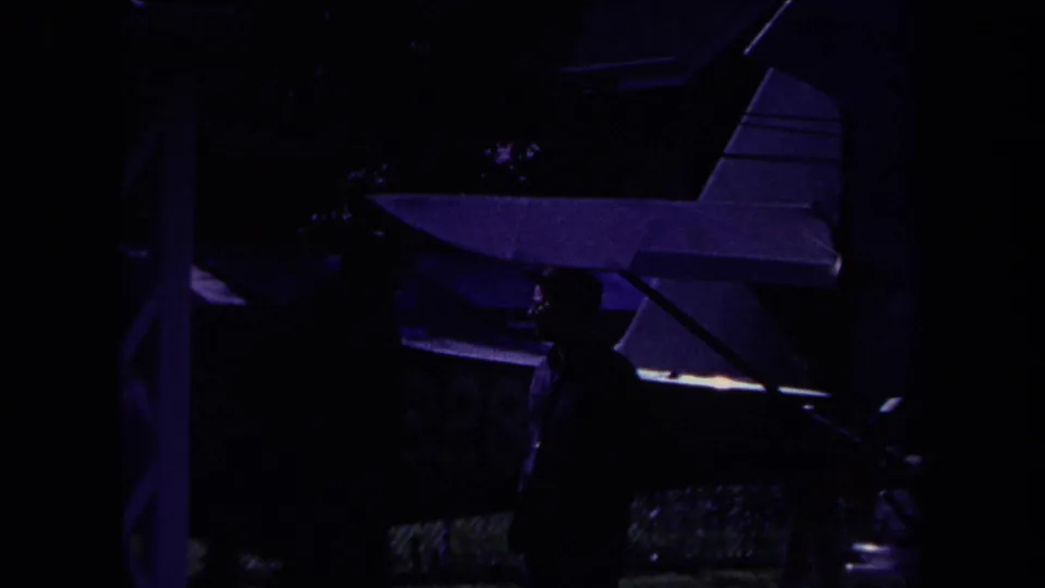 1969 Yucaipa home-movie frame showing a dark-suited man near a small airplane under low purple light.