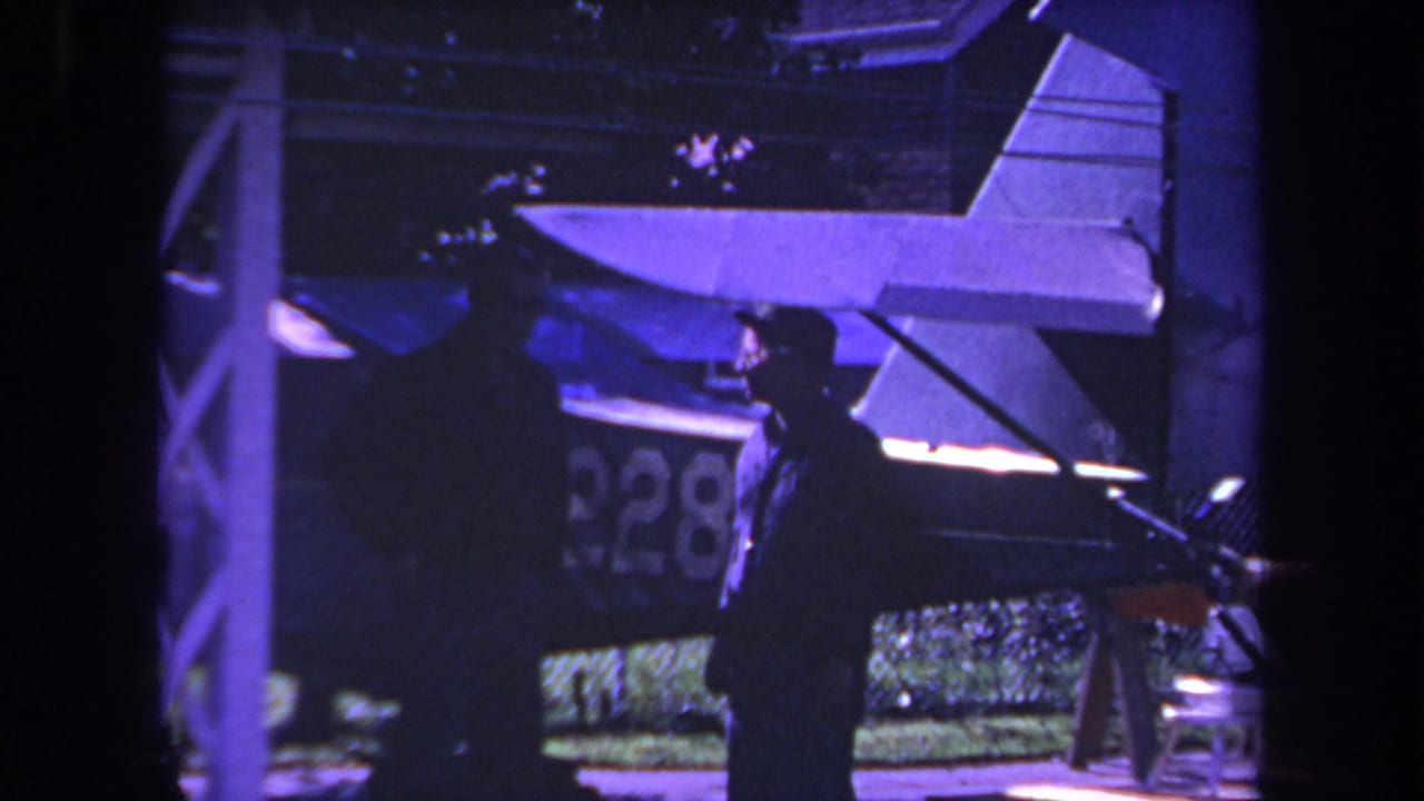 Man in hat stands near a small airplane with partial registration visible.