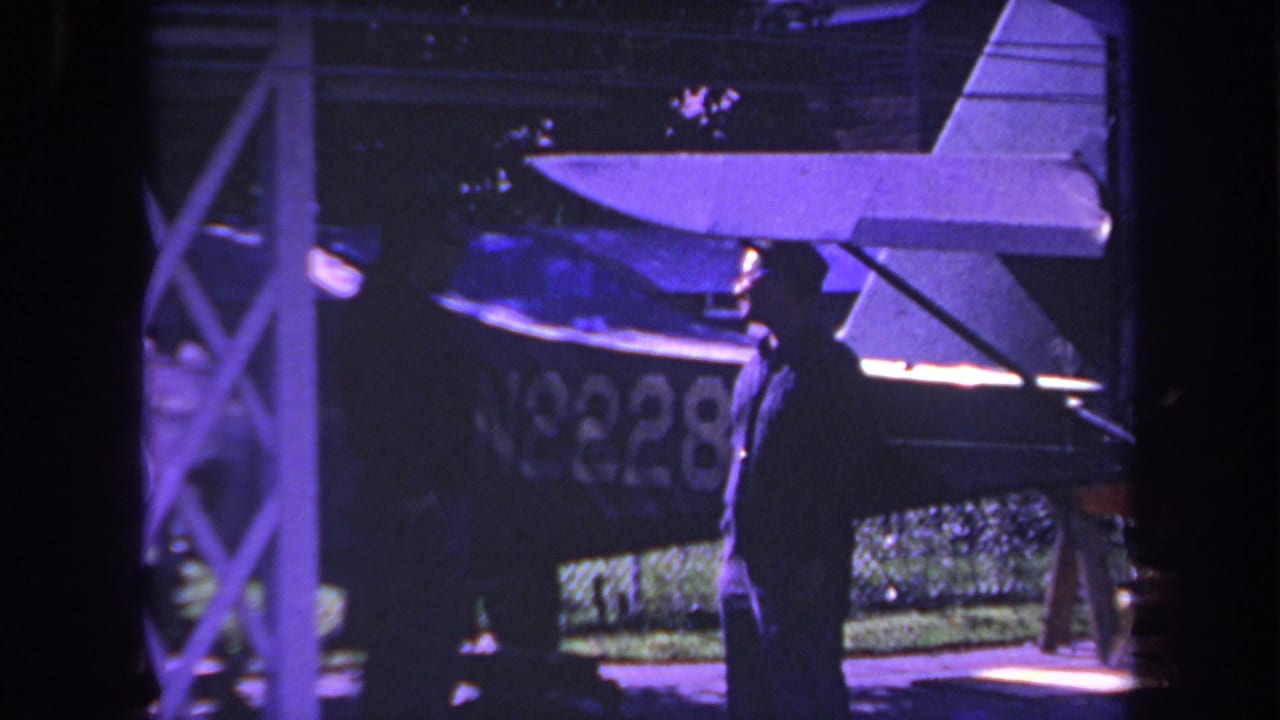 A silhouetted man faces another person beside the tail of a small aircraft.