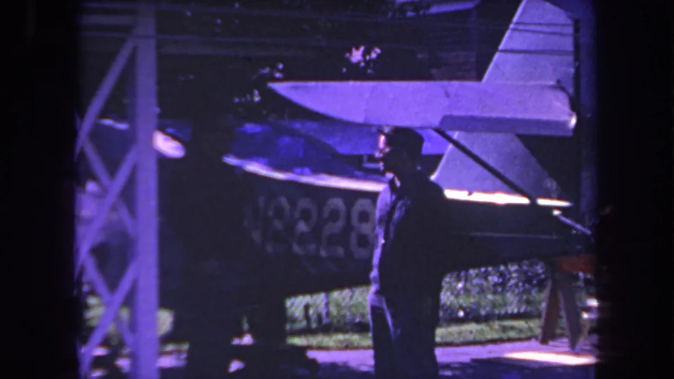 1969 Yucaipa home-movie frame showing two men conversing beside a small aircraft with N8228 partly readable.