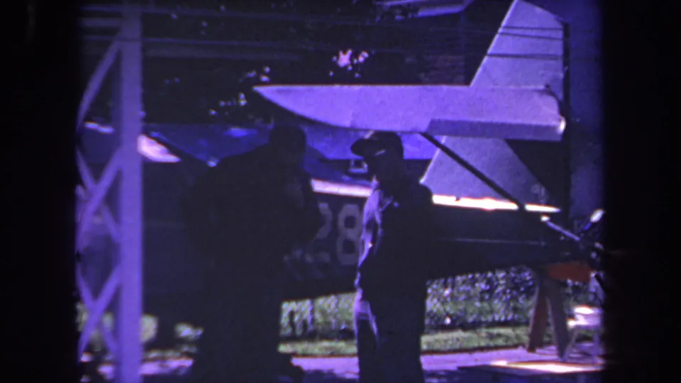 1969 Yucaipa 8mm frame showing two adults in silhouette near a small aircraft tail with a strong purple color cast.