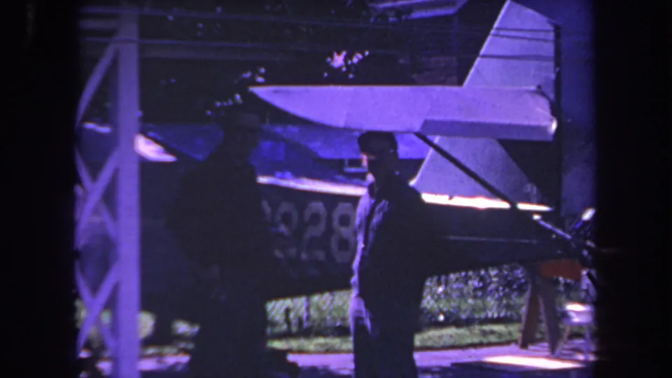 1969 Yucaipa home-movie frame with an adult in silhouette beside a small aircraft tail and partial aircraft marking.