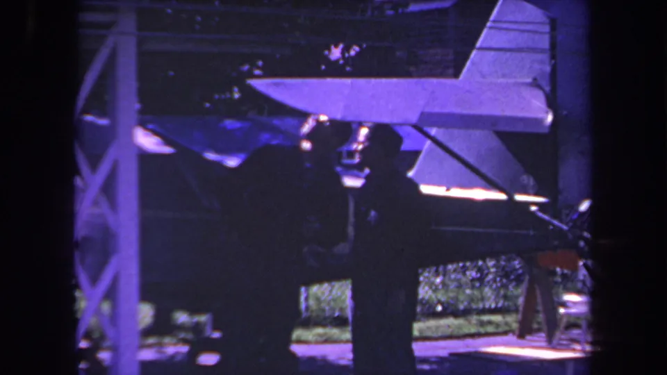 1969 Yucaipa 8mm frame showing two adults near the tail of a small aircraft, with heavy shadow and purple film shift.