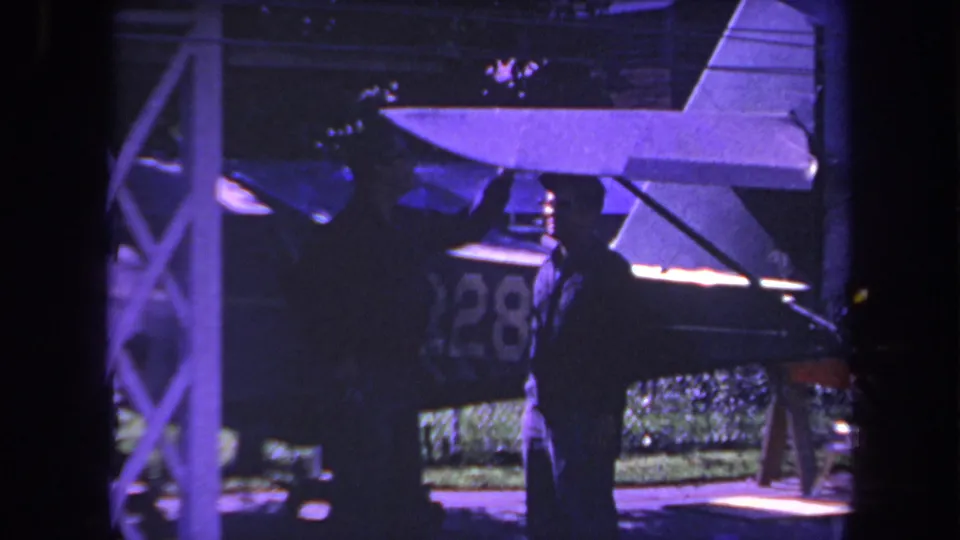 1969 Yucaipa 8mm frame of a silhouetted adult near a small aircraft tail, with partial number 28 visible in the background.