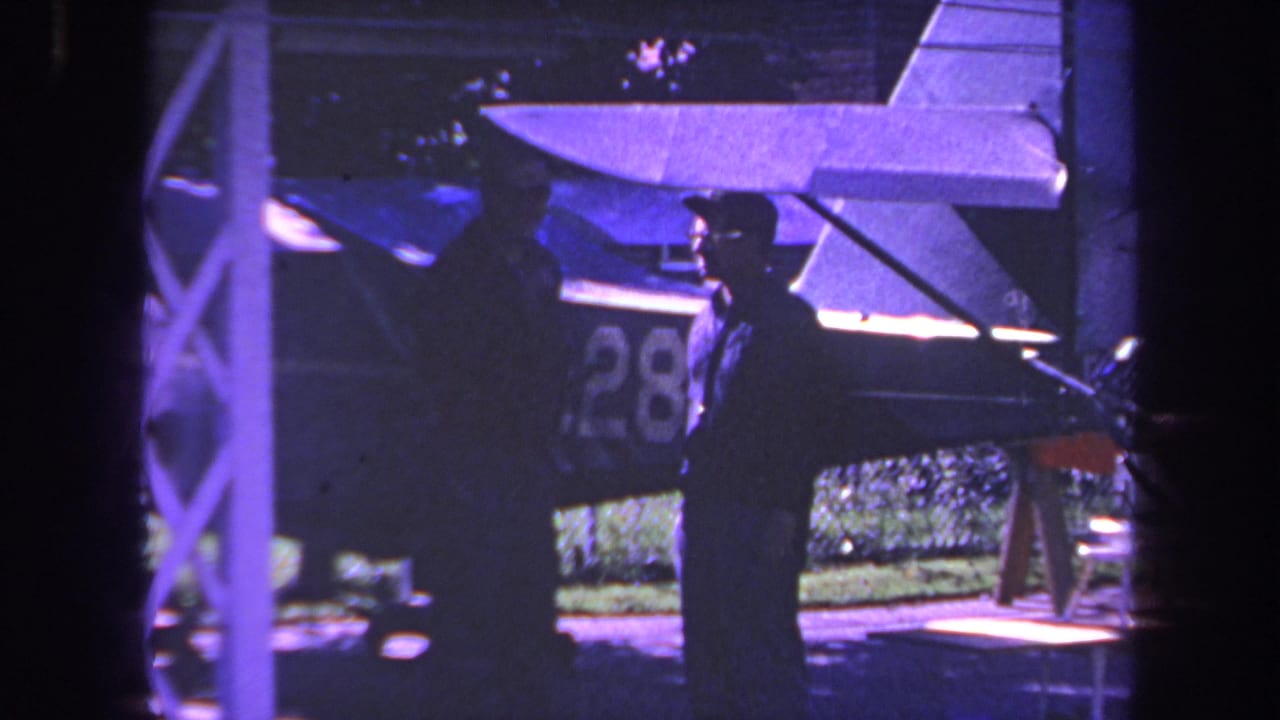 Two men remain beside the aircraft, with one near the wing and one in profile wearing sunglasses.