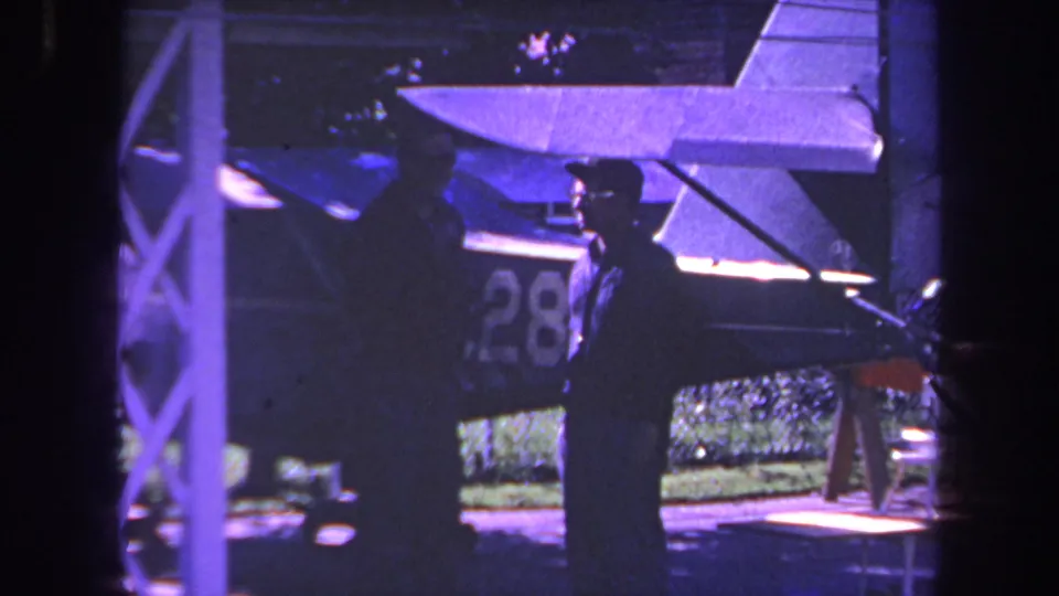 1969 Yucaipa-area frame of two adults beside a small aircraft, one partly under the wing and the other seen in dark profile near the fuselage number.
