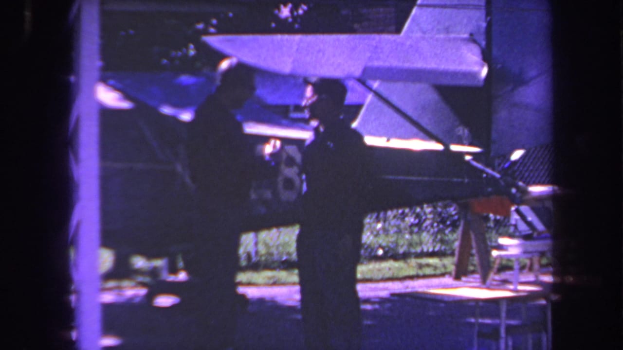 1969 Yucaipa home-movie frame showing two adult men near a small aircraft tail with a partial number visible on the fin.