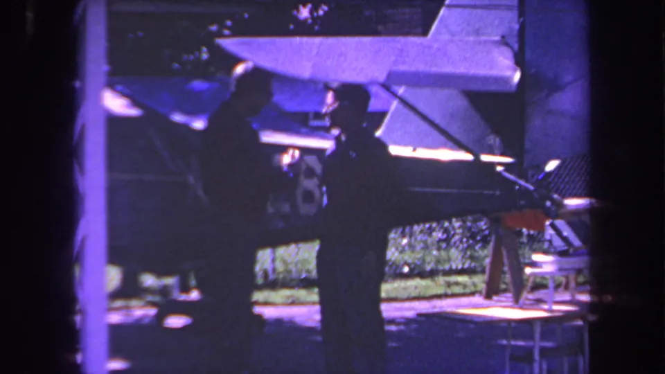 1969 Yucaipa home-movie frame showing two adult men near a small aircraft tail with a partial number visible on the fin.
