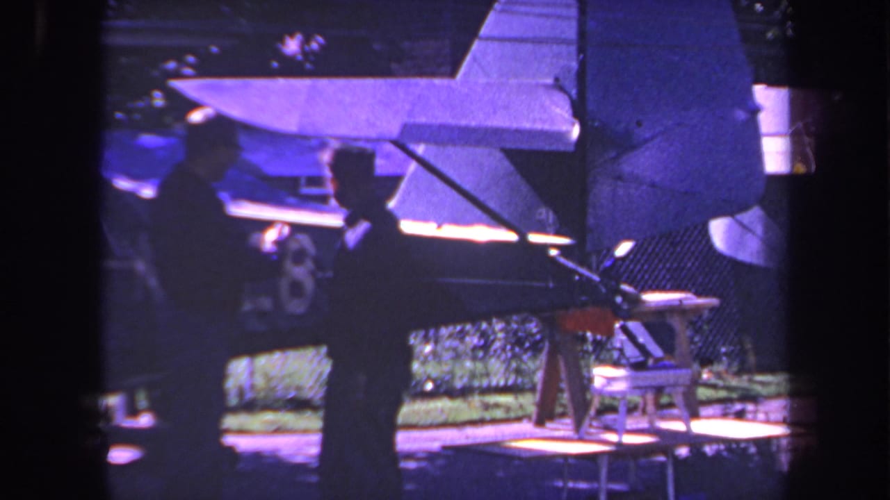 Two men are silhouetted near a small aircraft tail and rudder.
