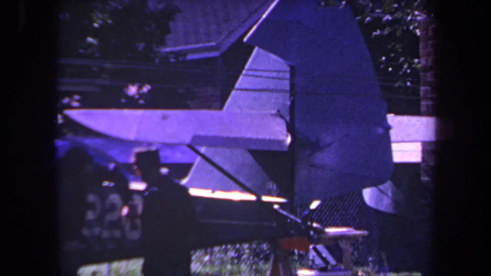1969 Yucaipa frame showing a man beside the small aircraft tail and rudder, with residential greenery in the background.