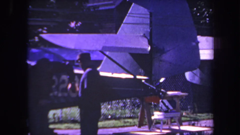 1969 Yucaipa 8mm frame showing two silhouetted men near a small propeller plane, with wing surfaces, fence, and greenery visible.