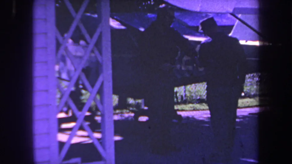 1969 Yucaipa home-movie frame with a silhouetted man beside a small propeller plane, partially obscured by foreground structure and low light.