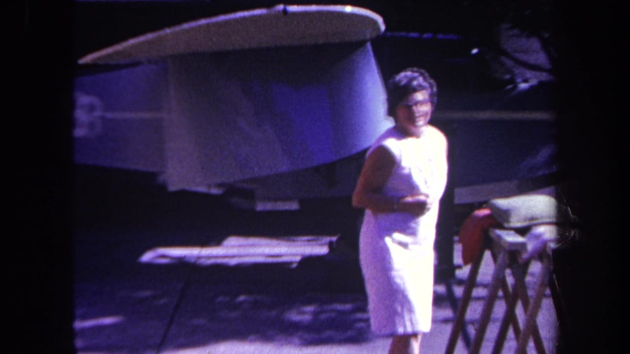 Woman in a white sleeveless dress stands outside near a large aircraft surface.