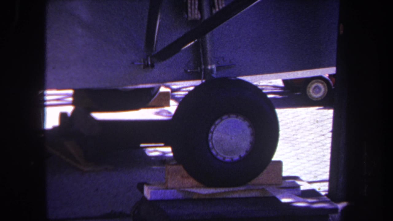 Trailer wheel beside wood blocks with undercarriage and railing in shadow.