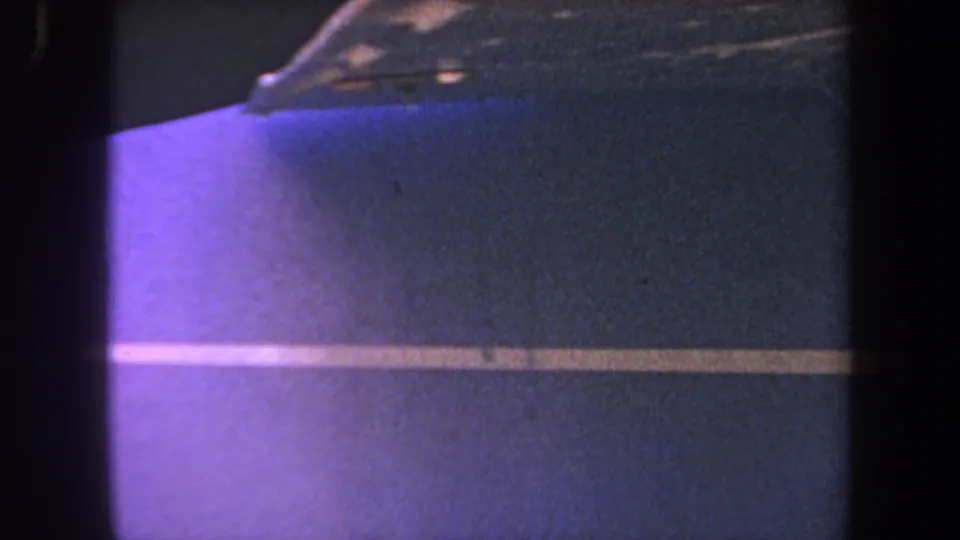 1969 8mm frame showing the blue aircraft body and yellow stripe from a close, low-light maintenance viewpoint.