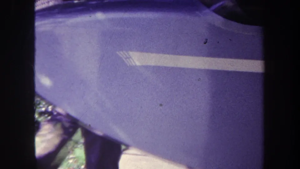 Close 1969 home-movie view of a blue curved vehicle or aircraft surface with a white stripe and grass beneath.