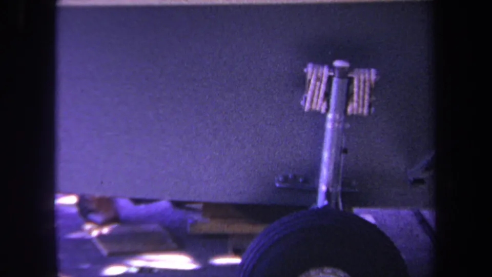 Close 8mm frame from Yucaipa showing a purple panel, landing-gear-like strut, wheel, and partial lower-edge objects.