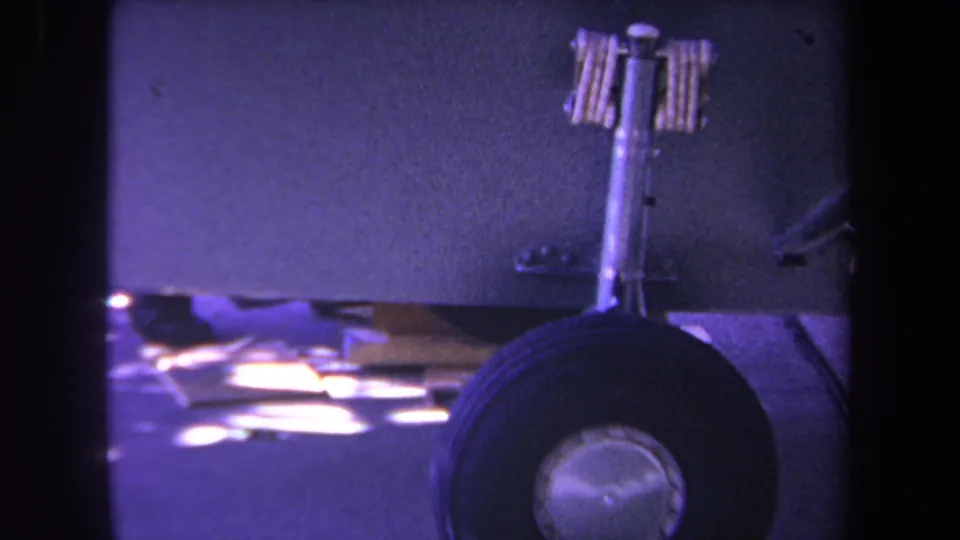 1969 Yucaipa home-movie frame showing a small private aircraft nose wheel, strut, and underside with a purple 8mm color cast.