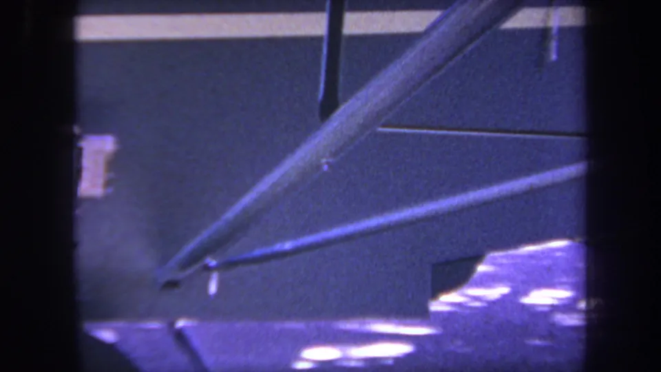 Close 8mm frame from the Yucaipa clip showing diagonal aircraft supports, underside panels, and partial landing gear area with purple color shift.
