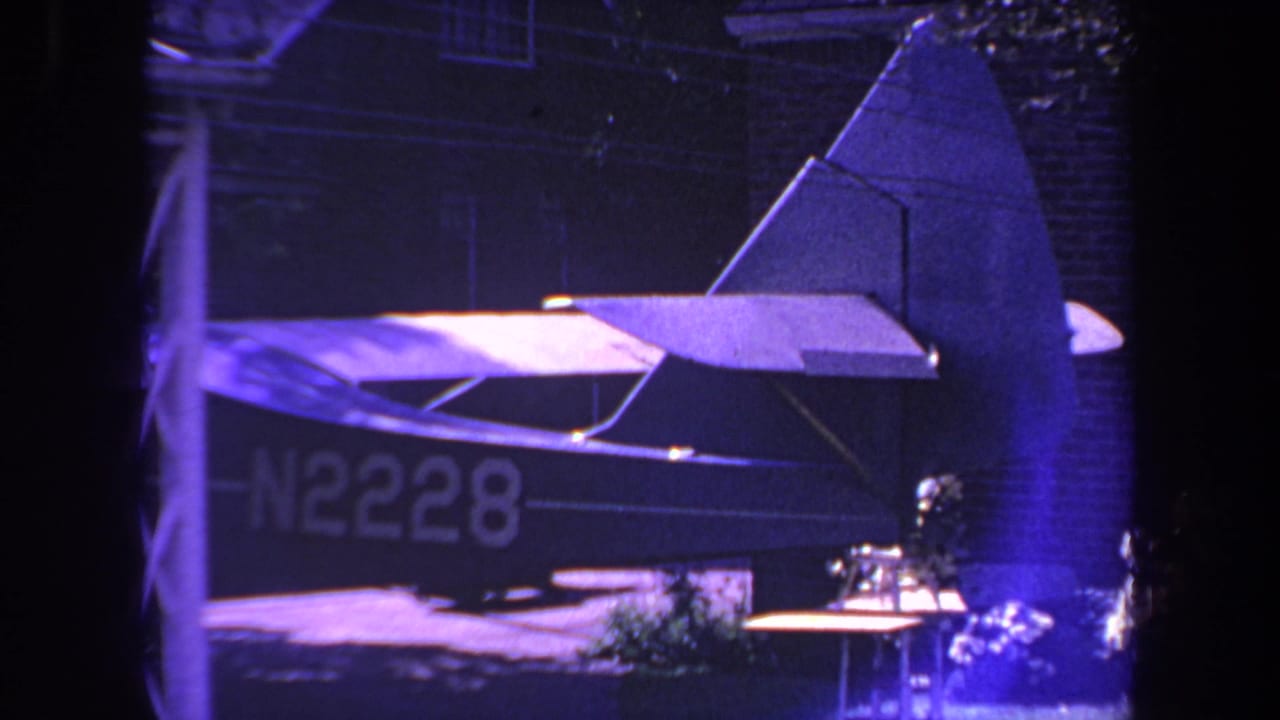Small airplane tail and rear fuselage marked N2228 beside a brick house at night.