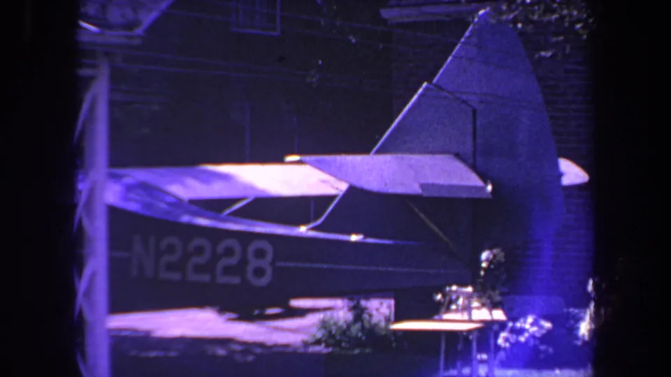 1969 Yucaipa home-movie frame showing the rear of a small airplane with registration N2228 near a brick residence under blue-purple light.