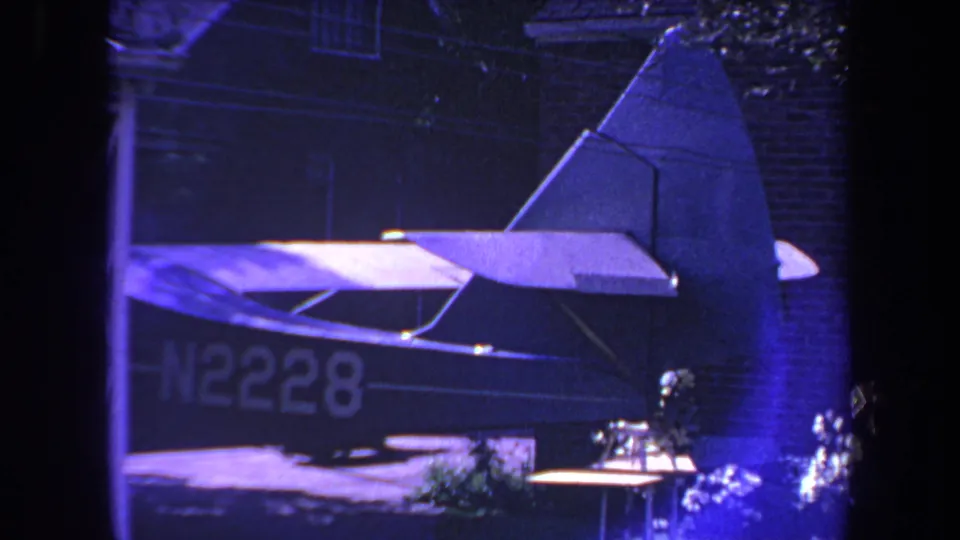 1969 Yucaipa frame of a small parked airplane with visible tail, rear fuselage, and N2228 registration near a brick residential exterior.