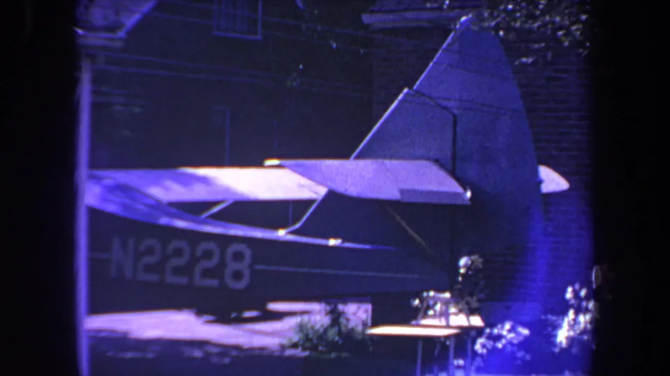 1969 Yucaipa home-movie frame showing the rear of a small airplane with registration N2228 near a brick residence under blue-purple lighting.