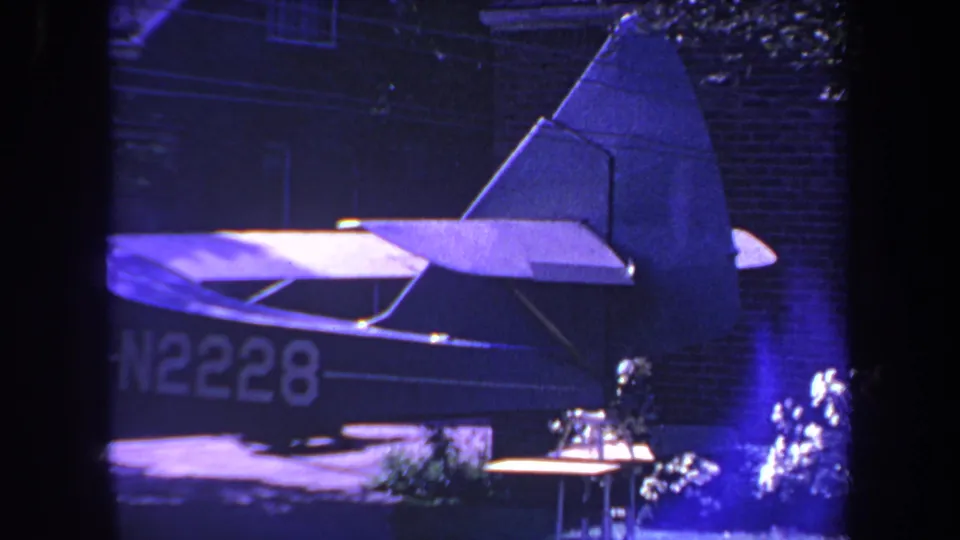 1969 Yucaipa frame with a small aircraft's tail, horizontal stabilizer, and partial N2228 marking beside a brick house and patio items.