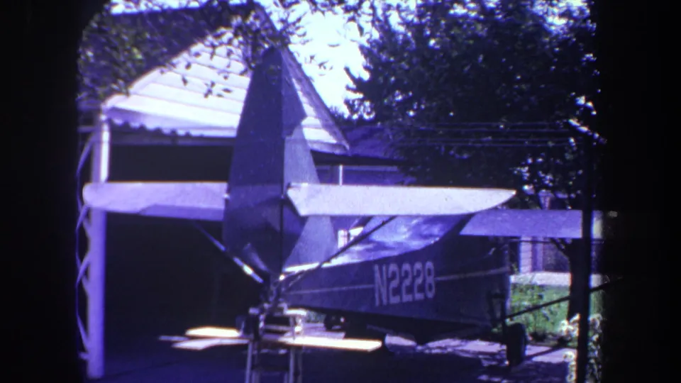 1969 Yucaipa frame showing the aircraft tail, wing, and N2228 marking outside or partly within a residential garage setting.