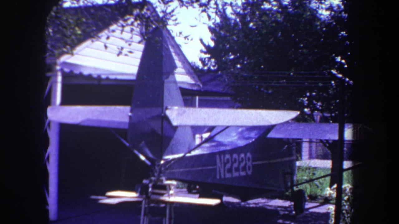Small high-wing airplane parked outside beside a house and trees.