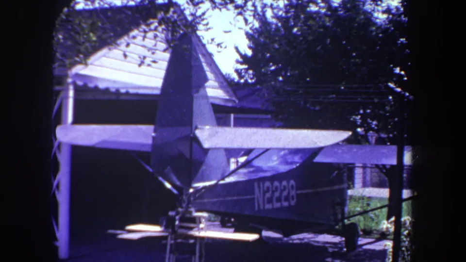 Small single-engine airplane marked N2228 parked outside in Yucaipa, California, with house roof and trees behind it.