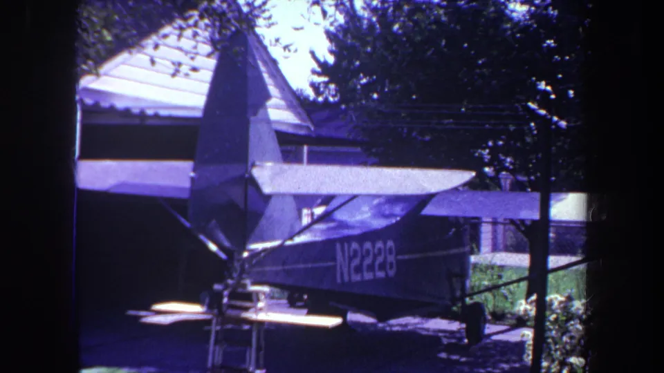 1969 8mm frame of a parked high-wing airplane in a residential outdoor setting in Yucaipa, California.