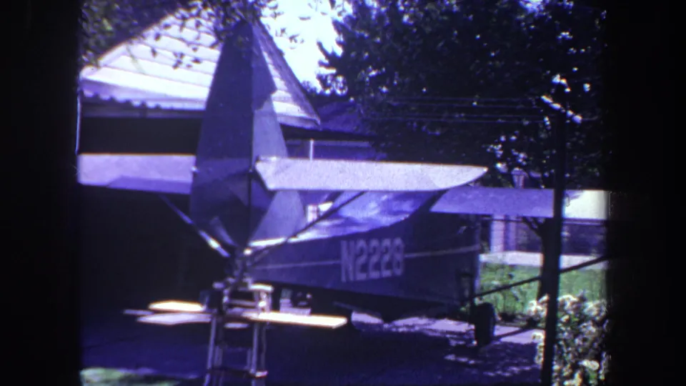 1969 Yucaipa home-movie frame showing a small airplane with registration N2228 parked in a residential driveway near a house and trees.