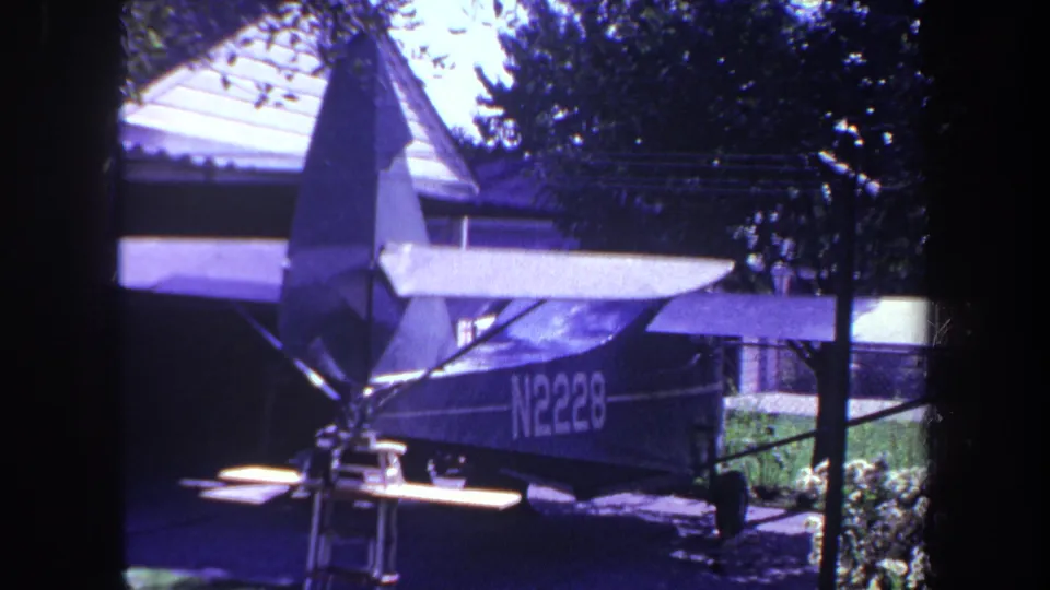 1969 Yucaipa frame of a high-wing tailwheel airplane parked in a driveway, with a house roof and trees behind it.