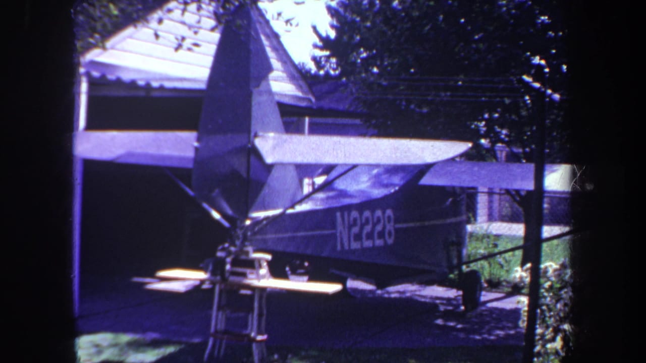 Small single-engine aircraft parked beside a garage in a yard.