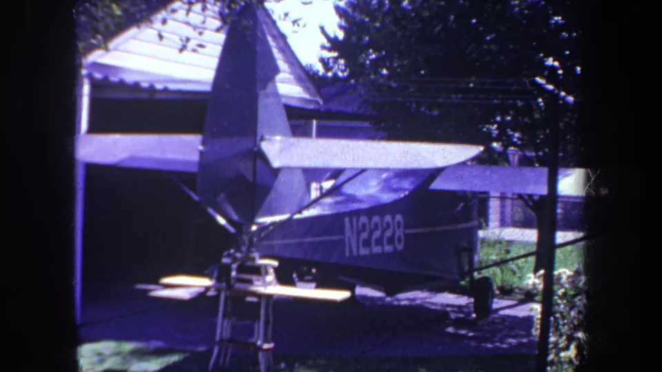 1969 8mm frame from Yucaipa, California, showing a small plane with registration N2228 parked near a garage and trees.