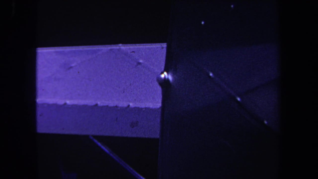 Close-up 8mm view of the aircraft's metal construction, with a wing edge and dark vertical structure in purple-tinted light.